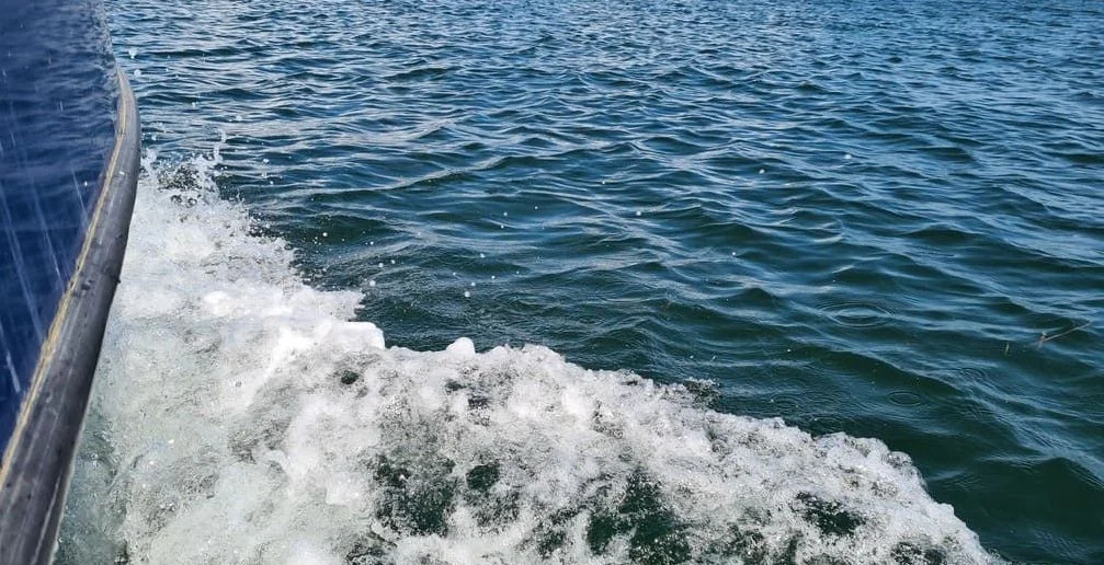 Boat hull edge with wake foam churning in blue-green water during operation.