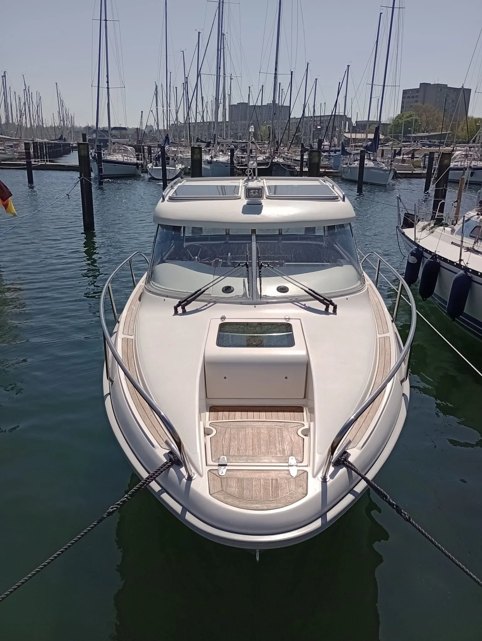 White recreational powerboat moored at marina dock in Cape Coral with sailboats in background.