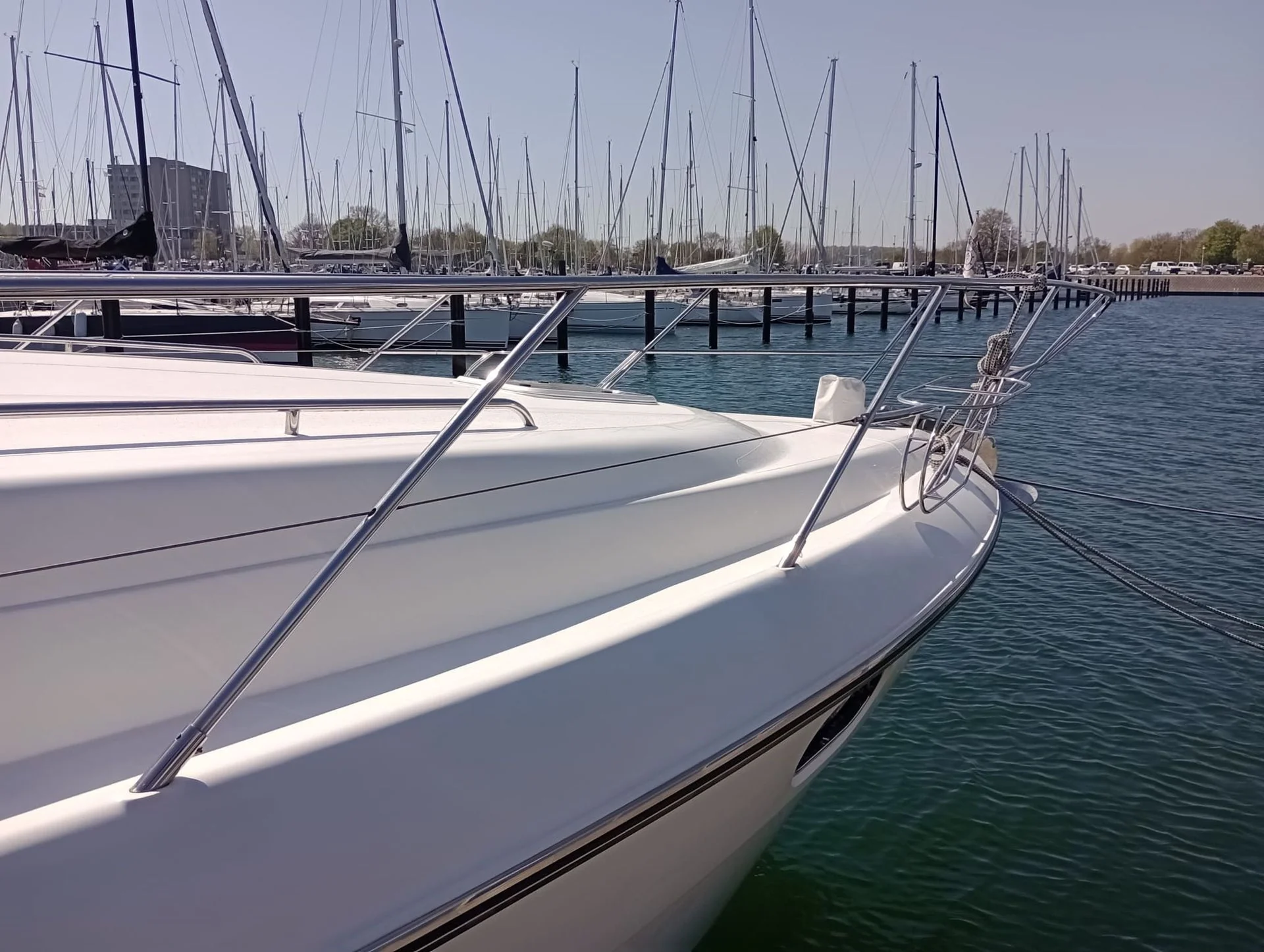 Row of moored sailboats with white hulls and rigging at a marina dock.