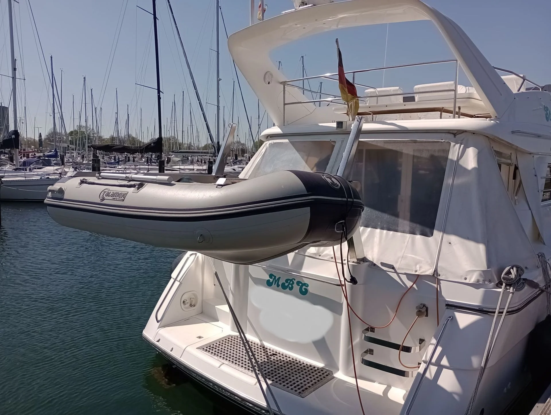 Recreational powerboat moored at marina with tender and sailboats in background.