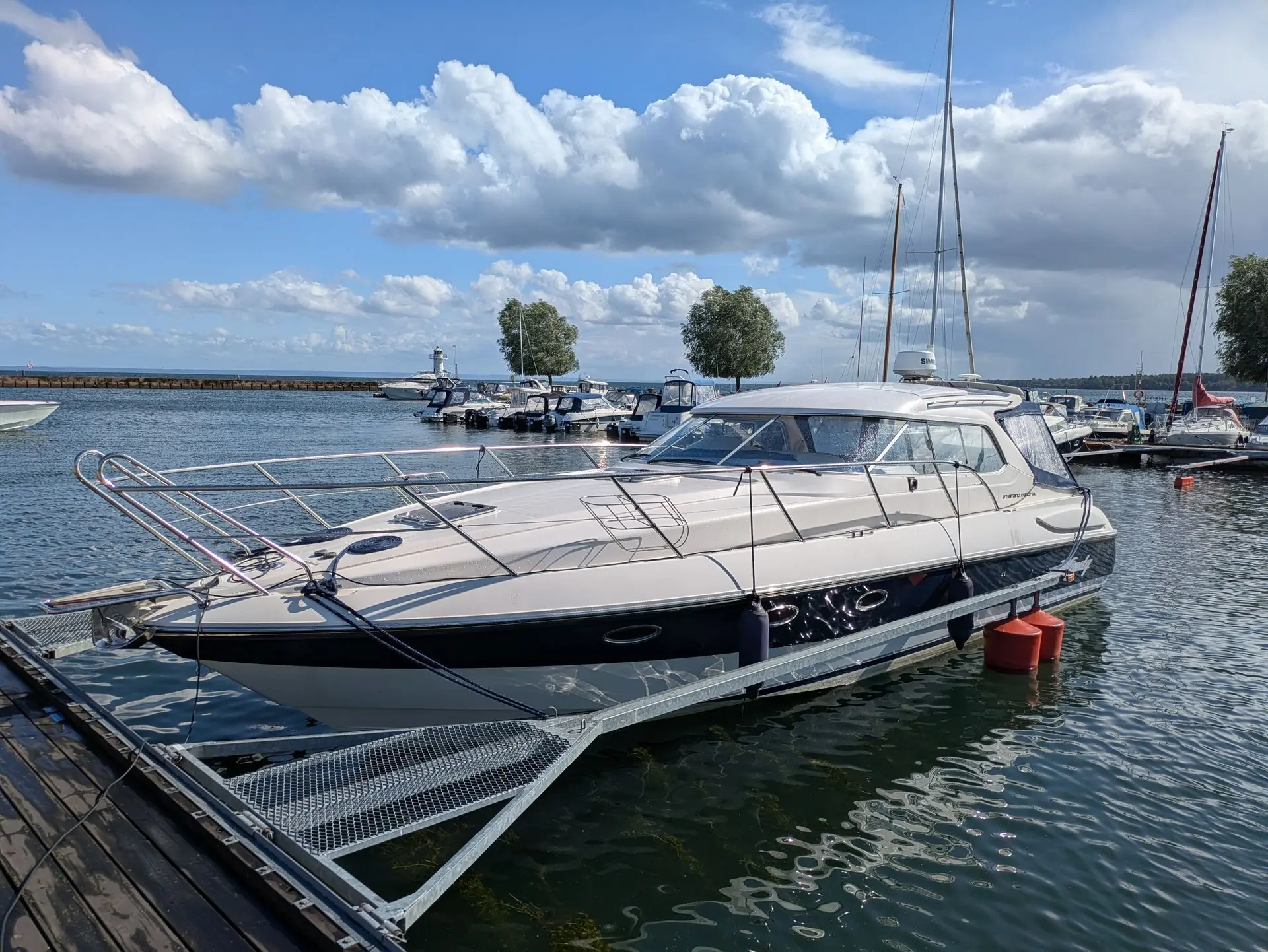 Recreational powerboat moored at Cape Coral marina dock with sailboats and waterfront in background.