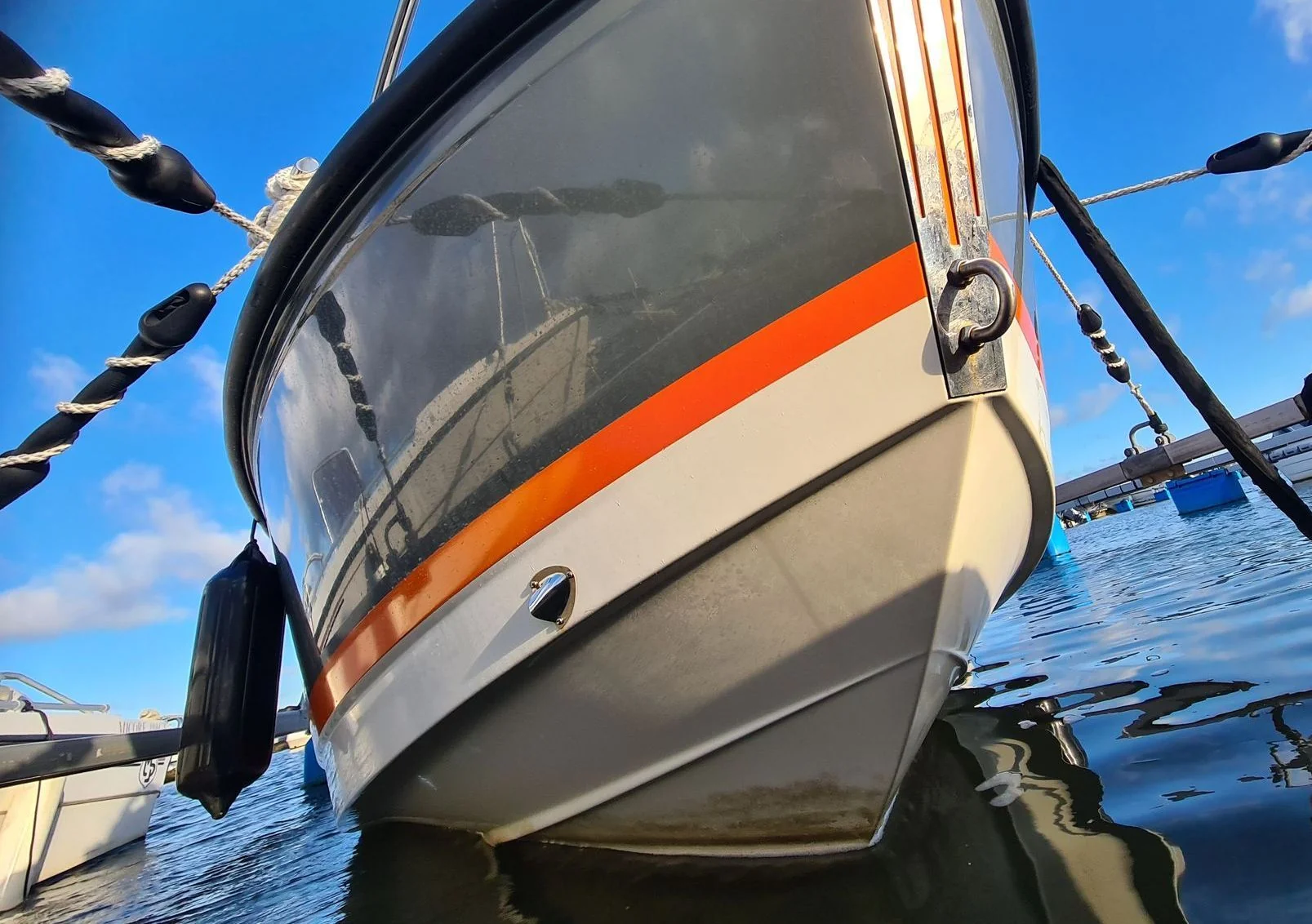 Recreational powerboat moored in calm water with orange stripe and rope rigging visible.