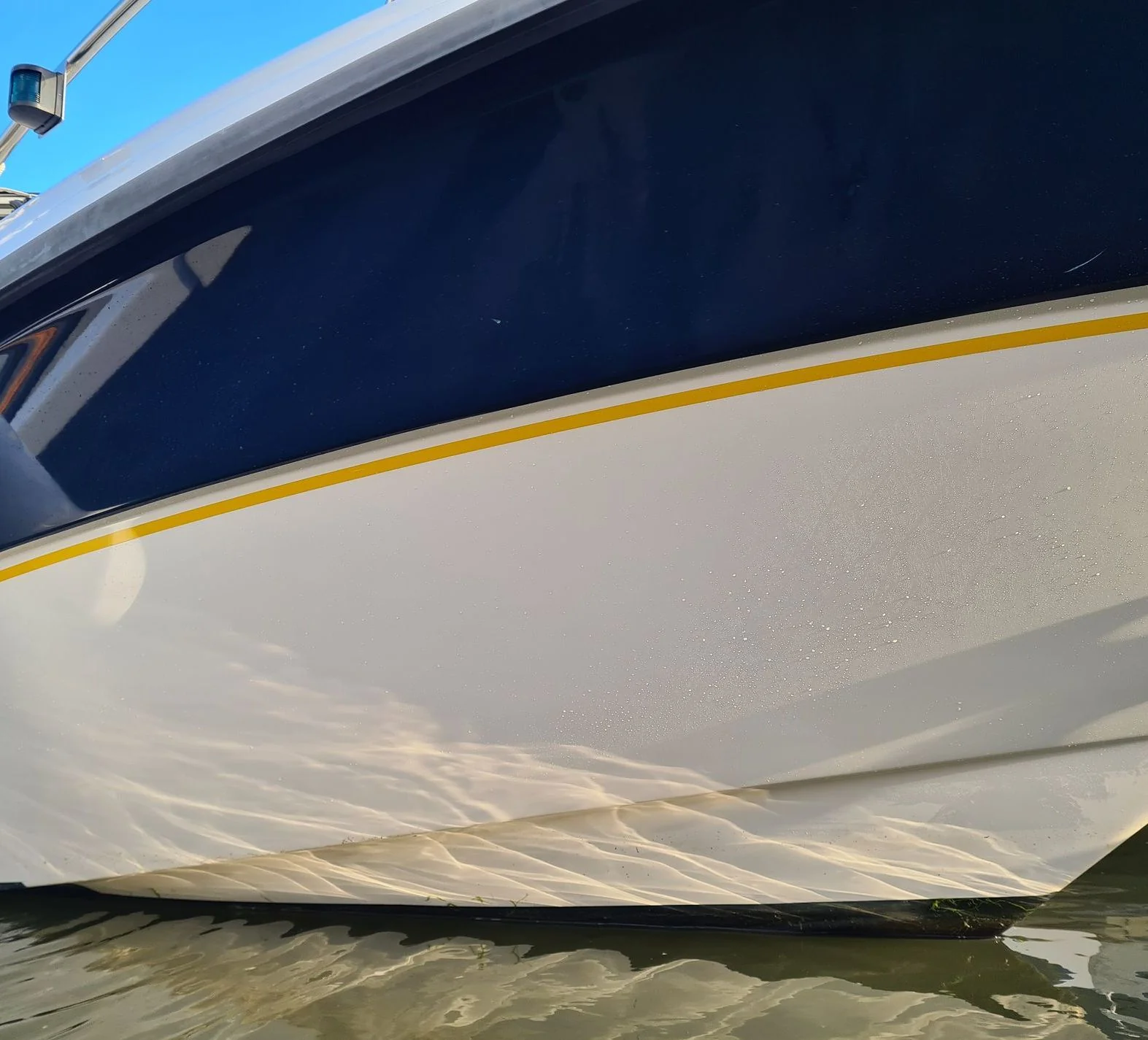 Boat hull detail showing canvas cover and yellow stripe trim in shallow water.