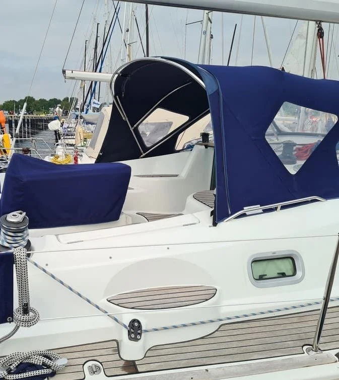 Sailboat with navy canvas canopy and white hull moored at marina dock.