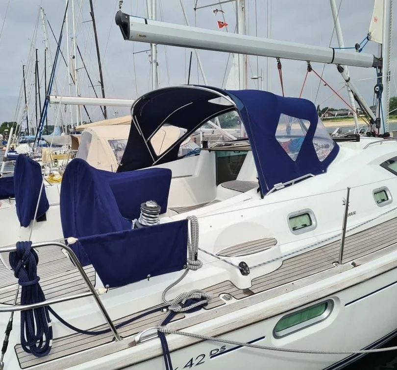 Sailboat with blue canvas canopy and white hull moored at marina dock.