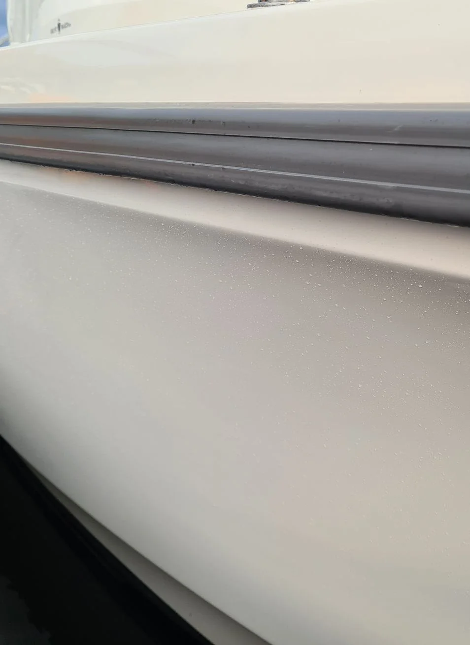 Close-up of boat hull gunwale showing white fiberglass surface with salt spray residue and dark trim.