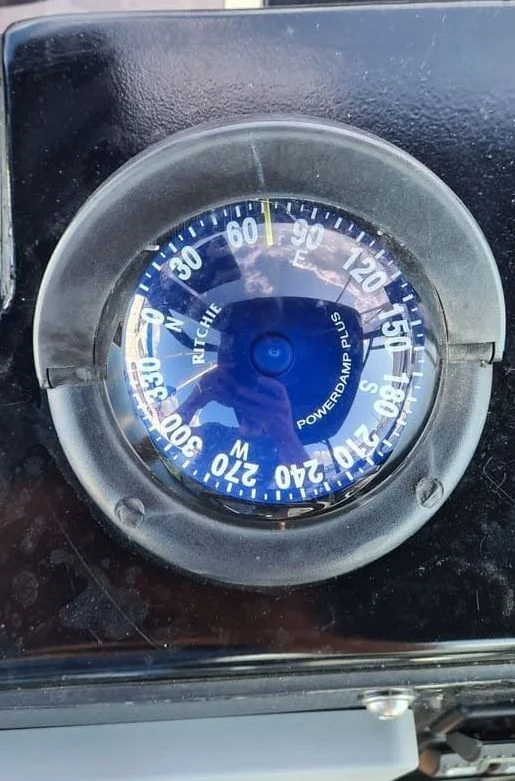 Marine compass gauge mounted on boat dashboard showing directional readings and powered indicator.