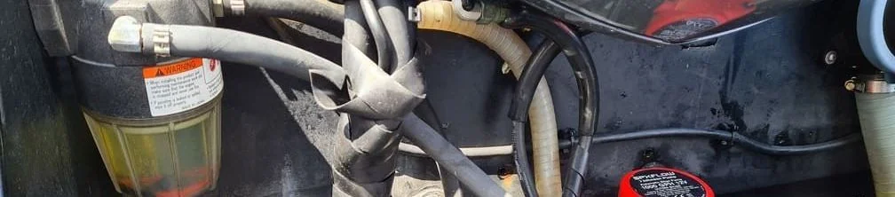 Close-up of marine engine fuel system components with weathered hoses and fittings during service inspection.