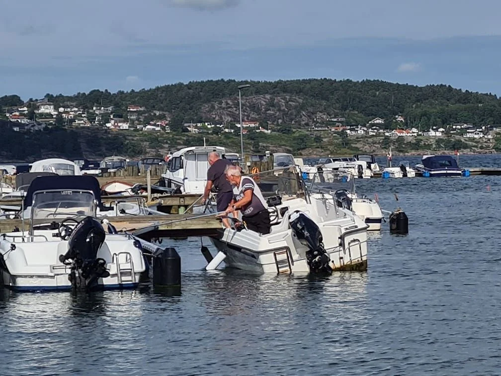 Mobile mechanic servicing outboard motor on recreational boat at waterside dock.