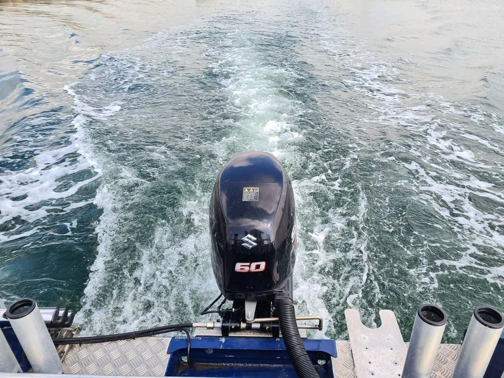 Outboard motor mounted on boat transom, viewed from helm during operation in open water.