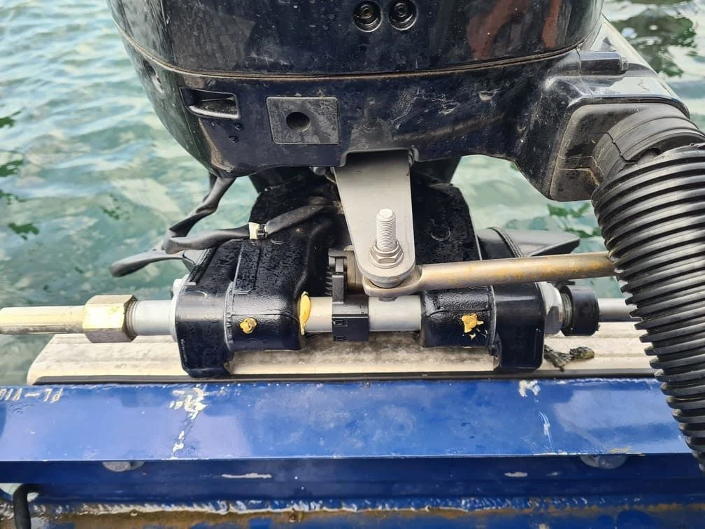 Outboard motor transom bracket assembly mounted on boat with water visible behind.