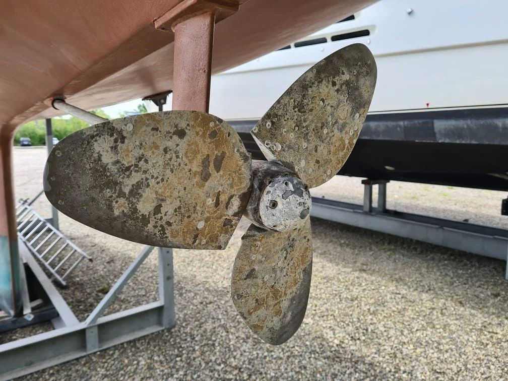 Corroded boat propeller with heavy marine growth and barnacle buildup under trailer.