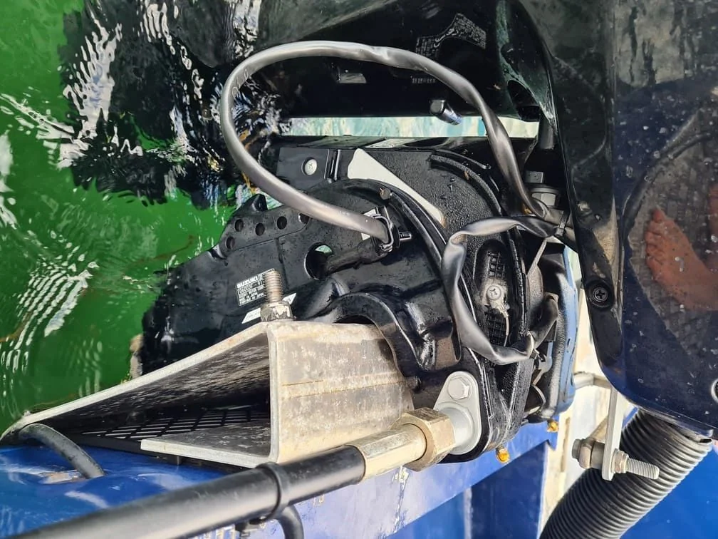 Outboard motor steering mechanism disassembled on boat, showing cable and hardware components.