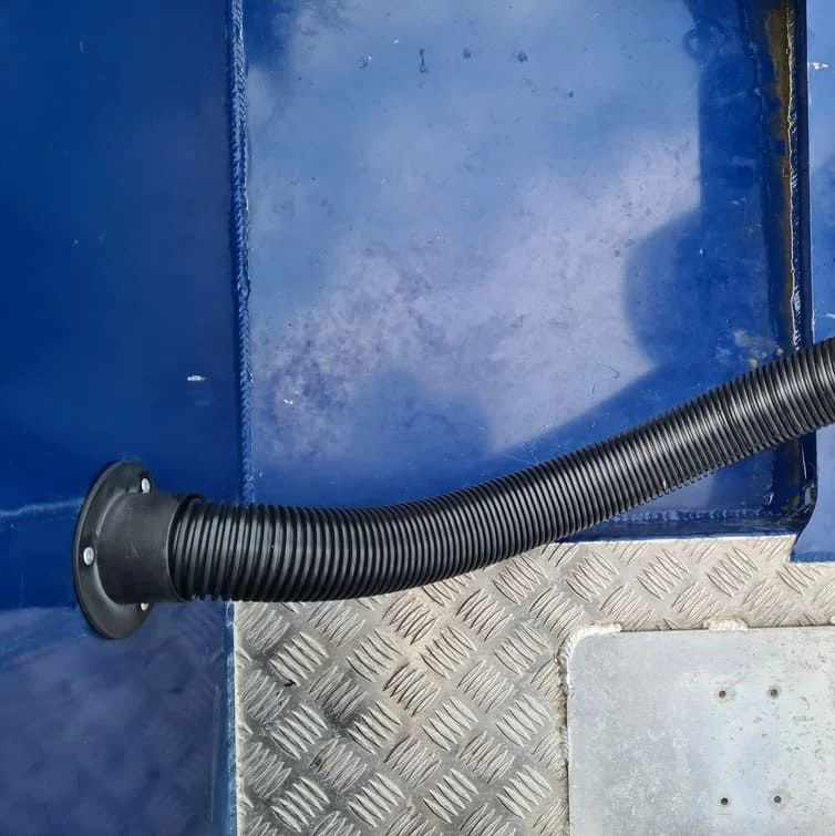 Flexible bilge hose connected to boat hull fitting with corrugated tubing and metal flange.